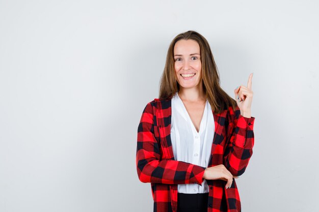 Jovem mulher com roupas casuais, apontando para cima e olhando alegre, vista frontal.