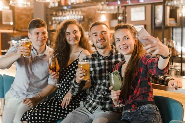 Jovem mulher com seus amigos segurando bebidas tomando selfie