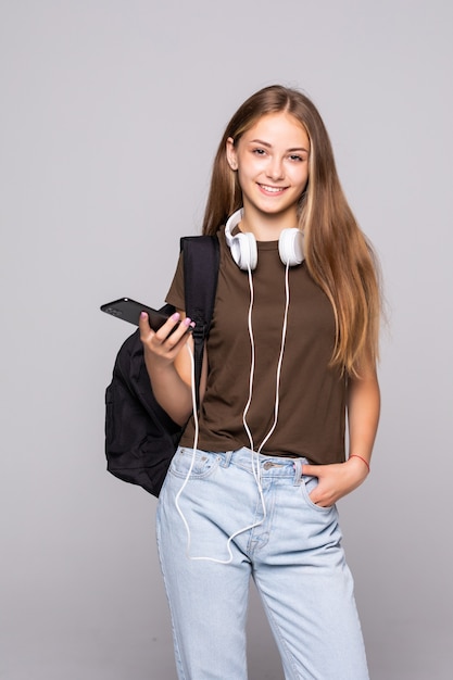 Jovem mulher com telefone inteligente ouve música com mochila isolada na parede branca