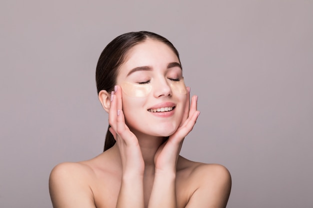 Jovem mulher com um tapa-olho tocando os templos isolados na parede cinza. Cosméticos, conceito de estresse de pele