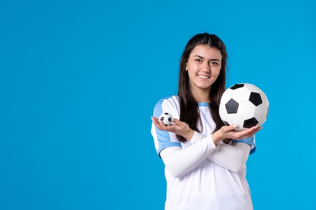 Jovem mulher com uma bola de futebol na parede azul de frente