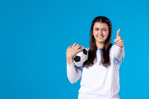 Jovem mulher com uma bola de futebol na parede azul de frente