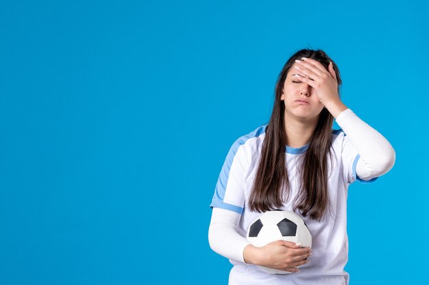 Jovem mulher com uma bola de futebol na parede azul de frente