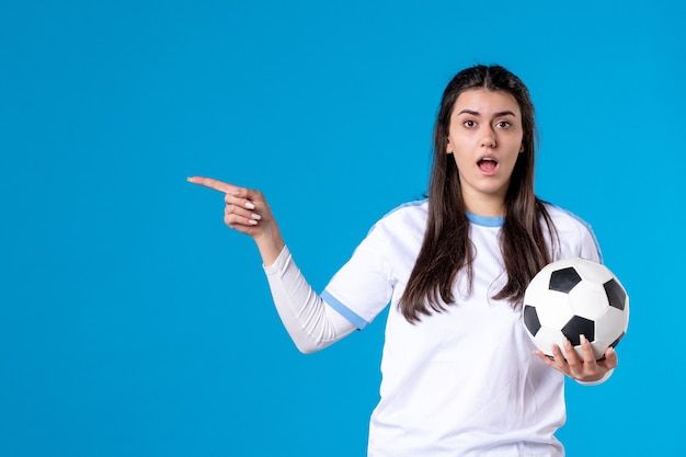 Jovem mulher com uma bola de futebol na parede azul de frente