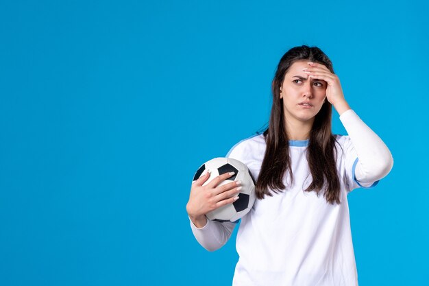 Jovem mulher com uma bola de futebol na parede azul de frente