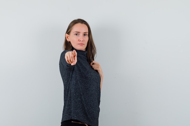 Jovem mulher com uma camisa, apontando para a câmera e parecendo confiante