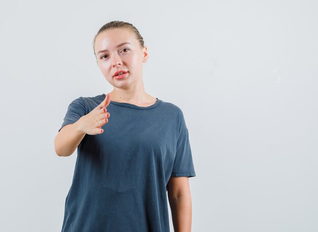 Jovem mulher com uma camiseta cinza esticando a mão para cumprimentar e parecer amigável