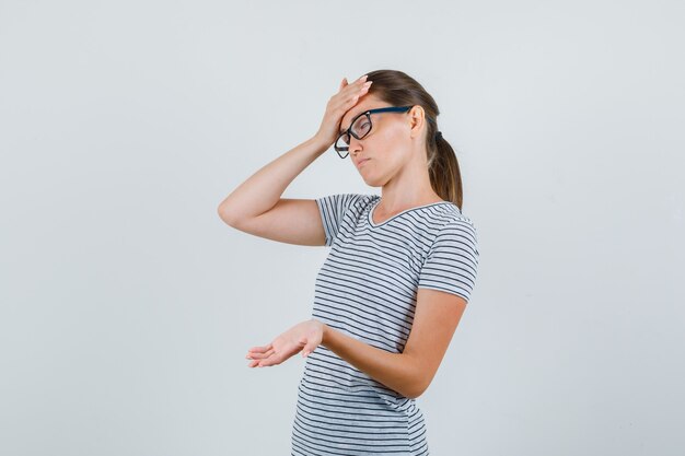 Jovem mulher com uma camiseta listrada, óculos mostrando a palma da mão e parecendo cansada, vista frontal.