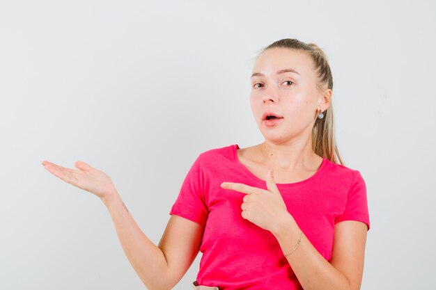 Jovem mulher com uma camiseta rosa apontando para o lado, fingindo segurar algo na palma da mão