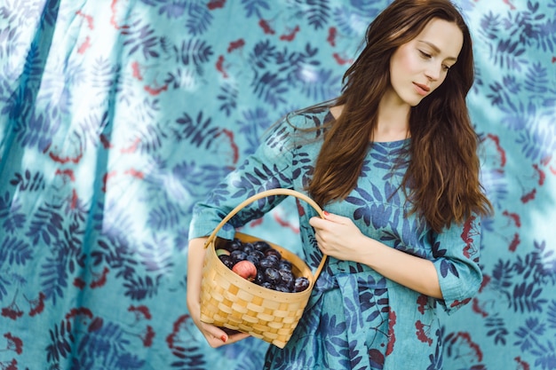 Jovem mulher com uma cesta de frutas, ameixas e maçãs.