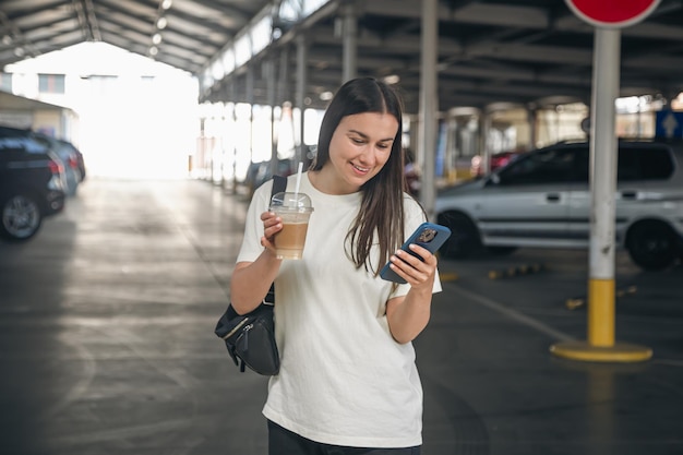 Jovem mulher com uma xícara de café no estacionamento esperando um táxi