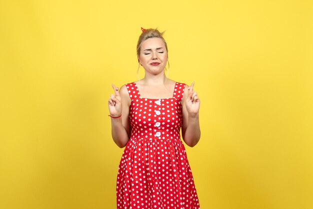 jovem mulher com vestido de bolinhas vermelhas cruzando os dedos no amarelo