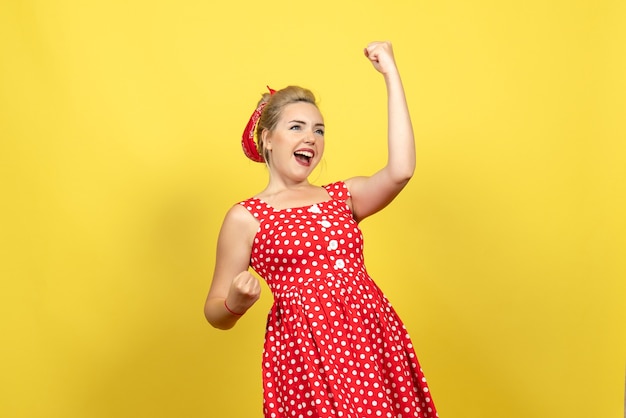 jovem mulher com vestido de bolinhas vermelhas posando emocionalmente em amarelo