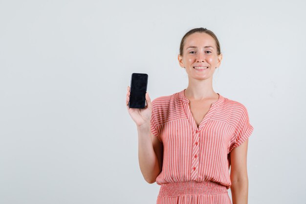 Jovem mulher com vestido listrado, segurando o telefone celular e olhando alegre, vista frontal.