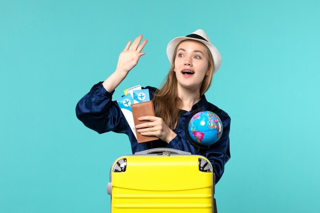 Jovem mulher com vista frontal segurando bilhetes e um globo na viagem de viagem de férias de avião de fundo azul