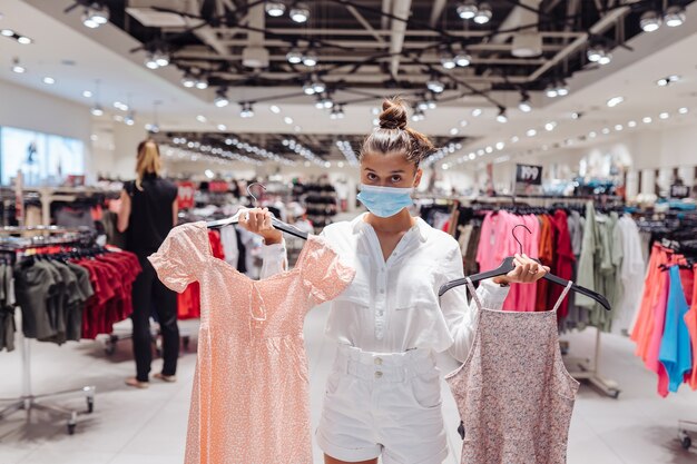 Jovem mulher comprando roupas em boutique de roupas com máscara protetora