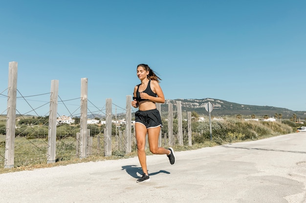 Foto grátis jovem mulher correndo ao longo da estrada a sorrir