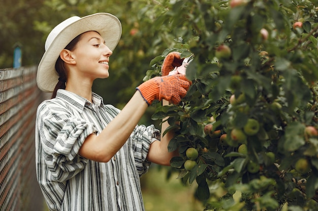 Foto grátis jovem mulher cuidando das plantas. morena com um chapéu e luvas. mulher usa aveeuncator.