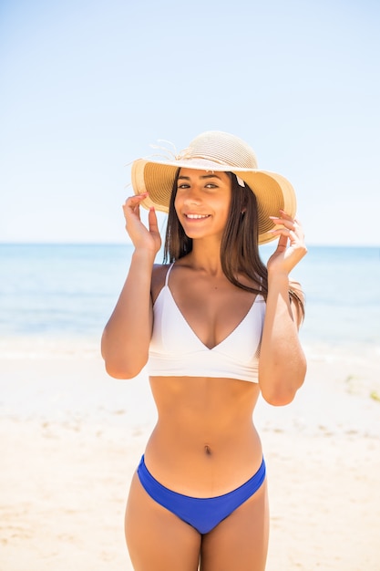 Foto grátis jovem mulher de biquíni com chapéu de palha branco, aproveitando as férias de verão na praia. retrato de uma linda mulher latina relaxante na praia com óculos de sol.