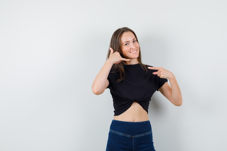 Foto grátis jovem mulher de blusa preta, calça mostrando gesto de me chamar e parecendo alegre