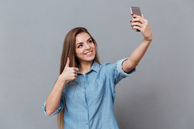 Jovem mulher de camisa fazendo selfie em smartphone