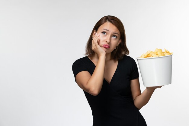 Jovem mulher de camisa preta segurando batatas fritas e pensando na superfície branca de frente