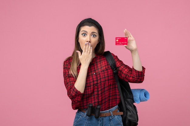 Jovem mulher de camisa vermelha com cartão do banco em um fundo rosa mulher cor de frente