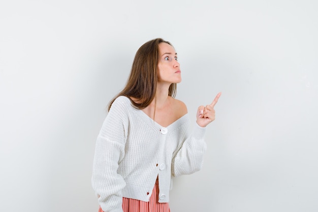 Foto grátis jovem mulher de casaco e saia apontando para o canto superior direito e parecendo zangada isolada