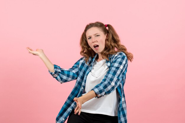 Jovem mulher de frente, com camisa quadriculada azul dançando na parede rosa jovem modelo emoções mulher criança menina