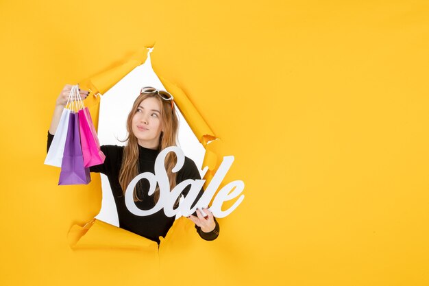Jovem mulher de moda com sacos de compras através de um buraco de papel rasgado na parede