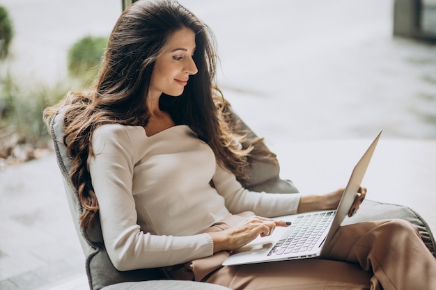 Foto grátis jovem mulher de negócios sentada em uma cahir trabalhando no computador