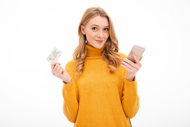 Jovem mulher de sorriso que guarda o telefone móvel e o cartão de crédito.