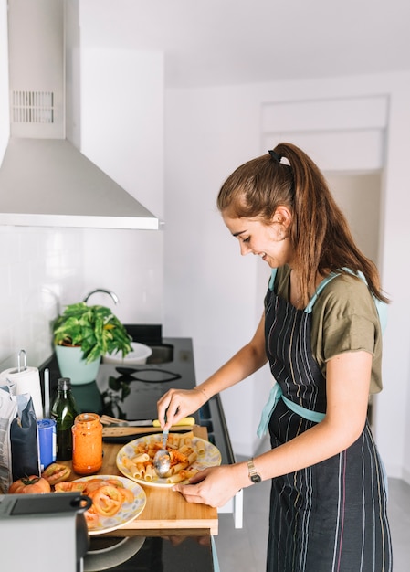 Foto grátis jovem mulher de sorriso que prepara a massa do rigatoni na cozinha