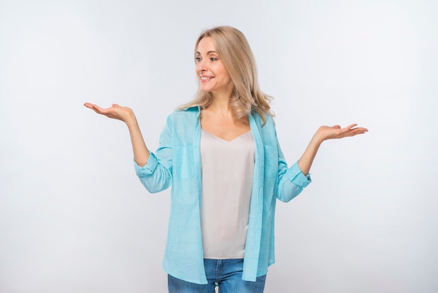 Jovem mulher de sorriso que shrugging isolado de encontro ao fundo branco