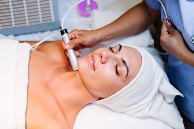 Jovem mulher deitada na mesa do cosmetologista durante o procedimento de rejuvenescimento