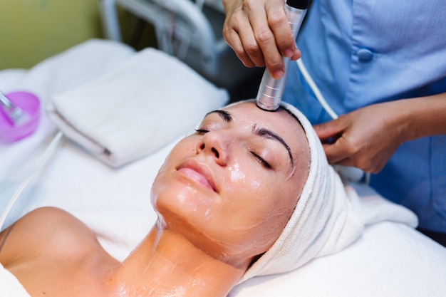 Jovem mulher deitada na mesa do cosmetologista durante o procedimento de rejuvenescimento