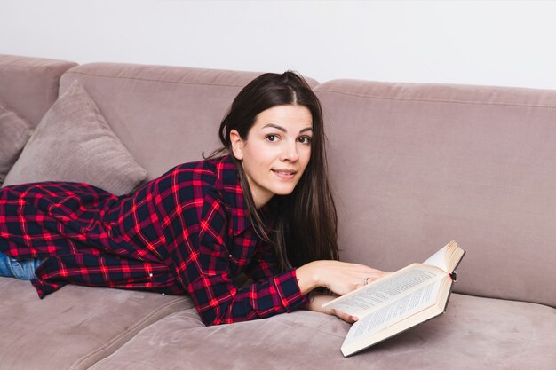 Foto grátis jovem mulher deitada no sofá a ler o livro a sorrir