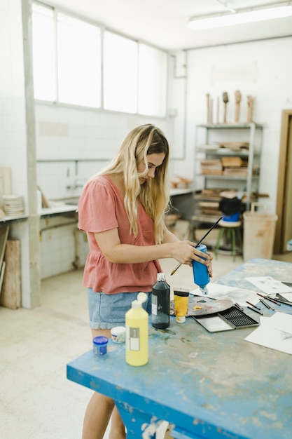 Foto grátis jovem mulher derramando aquarela de garrafa na bancada