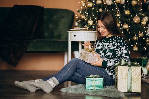 Jovem mulher desembalar presente de Natal pela árvore de Natal