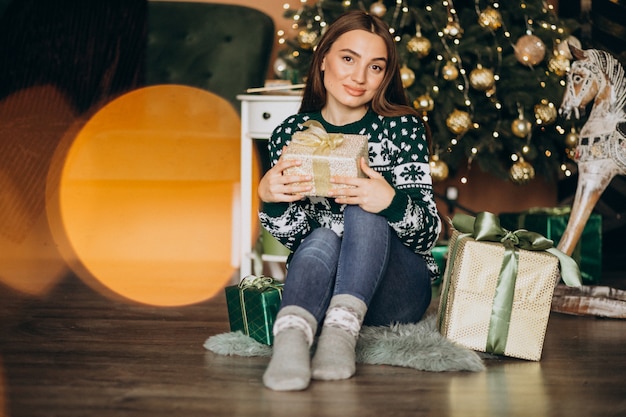 Jovem mulher desembalar presente de natal pela árvore de natal