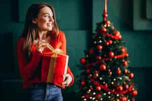 Foto grátis jovem mulher desembalar presente de natal pela árvore de natal