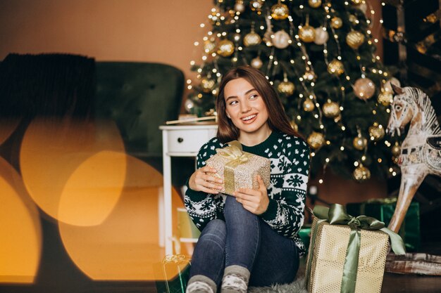 Jovem mulher desembalar presente de Natal pela árvore de Natal