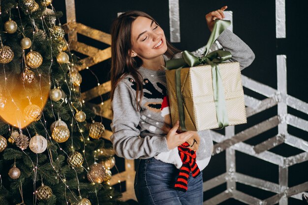 Jovem mulher desembalar presente de Natal pela árvore de Natal