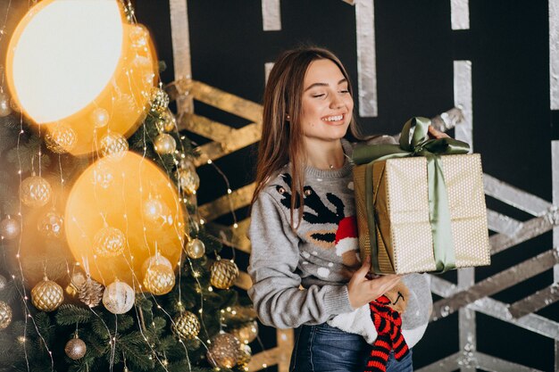 Jovem mulher desembalar presente de Natal pela árvore de Natal