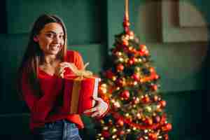 Foto grátis jovem mulher desembalar presente de natal pela árvore de natal