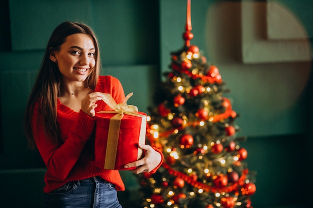 Jovem mulher desembalar presente de Natal pela árvore de Natal