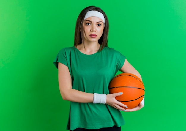 Jovem mulher desportiva com bandana e pulseiras, segurando uma bola de basquete e olhando