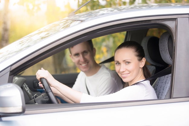 Jovem mulher dirigindo, um homem sentado perto do carro