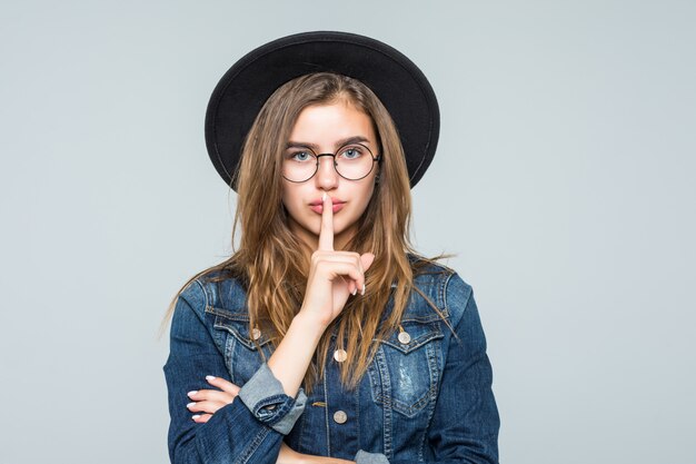 Jovem mulher do retrato que mostra o gesto do silêncio sobre o fundo cinzento