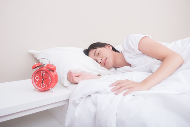 Foto grátis jovem mulher dormindo na cama ao lado do despertador